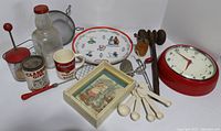 Overview of all red kitchen items in the lot including clock, measuring spoons, utensils, decorative plate, glassware, and collectibles.