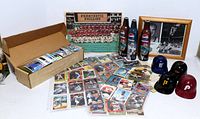 Box containing assorted baseball cards, loose cards spread around, four plastic baseball helmet caps, three football-themed Pepsi bottles, framed Philadelphia Phillies team photo