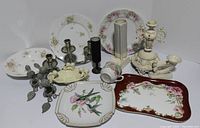 Wide view of lot showing floral porcelain plates, a bridal white ornate angel planter, various candlesticks, metal bird napkin rings, cherub soap dish, and decorative platter.