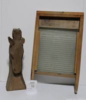 Photo of wood carved horse head sculpture next to glass washboard showing both items and their relative size.