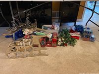 Photo showing the silver-tone metal reindeer shaped holder, assorted Christmas decorations including greenery with poinsettia flowers, blue tinsel garland, packaging of lights and ornaments, bows and wreath hangers.