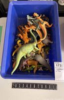 Top-down view of blue plastic bin filled with various plastic dinosaur toys in multiple colors.