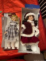 Photo showing two dolls in their respective boxes: one Symphony Doll dressed in plaid and white, and one Christmas doll dressed in red and white festive attire.