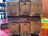 Nine pairs of metal earrings displayed on a table in original packaging with visible intricate metalwork and different shapes.