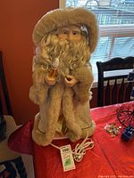 Front view of Saint Nicholas figure with cream fur-trimmed coat and hat, holding light, placed on table near window.