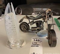 Glass sculpture of Burj Dubai building with built-in light alongside a metal Indian motorcycle sculpture with spring and bolt details.