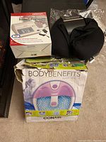 Photo showing Omron blood pressure monitor box, Conair Body Benefits foot spa box, and black hooded microbeads travel neck pillow on floor.