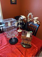 Five jewellery display items including a plexiglass display case and four jewellery stands on a table with red cloth.