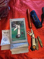 Photo showing two multi purpose golf tools, an orange flashlight, a blue flashlight, and the box for one golf tool labeled 'All Purpose Golf Tool'.