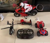 Radio-controlled Ducati motorcycle with rider figure, black helicopter, red ATV, and three controllers on a white surface.