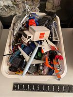 Various toy vehicles including cars, trucks, and planes piled in a white plastic basket showing different types and colors.