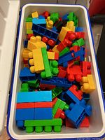Colorful plastic Mega Bloks building blocks assorted by color and size inside a white storage container.