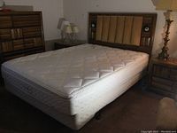 Full view of queen-sized bed frame with mattress and box spring under ambient room lighting showing mattress with stains.