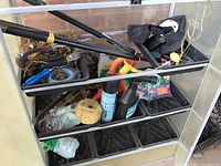 Overhead view showing assorted gardening tools, clippers, pruners, twine, knee pads, and yard chemical containers inside large clam shell planters.