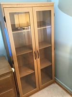 Front view of wooden display cabinet with glass doors, showing interior shelves and black handles.