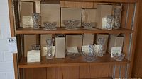 Wide shot of 11 Lenox crystal candy bowls and vases displayed on wood shelves with original boxes and certificates visible.