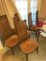 Eight wooden dining chairs including six standard and two captain's chairs shown grouped in a room with curtain backdrop.