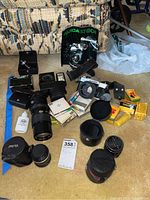 Full lot overview with camera, lenses, lens cases, right angle finder, flash, and film arranged on floor with seller tag visible