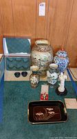 Displays entire lot with various sized Asian styled ceramic vases, ginger jar with lid, white figurine, black tray, tea cups, coaster, and box