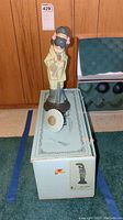 Photo of Lladro figurine on top of original box showing full front view, figurine standing with umbrella placed beside base.