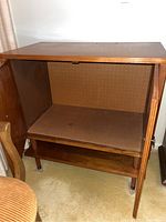 Open cabinet showing interior pegboard backing and lower shelf, mid-century modern style legs.