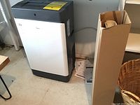 Full side and front view of Midea portable air conditioner in basement area with document and cardboard box beside it.