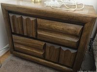 Front view of one nightstand showing sculpted drawer fronts and brown wood veneer finish