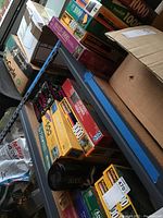 Photo showing multiple boxed puzzles stacked on metal storage shelves, various brands and designs visible, unopened and opened boxes present.