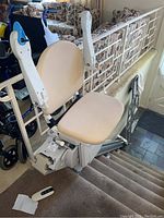Overview of beige stair lift chair mounted on straight rail track with handheld remote placed on floor