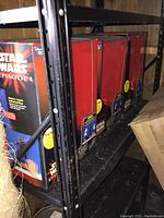 Side view of three boxed Star Wars Episode I talking banks on a metal shelf in storage environment.