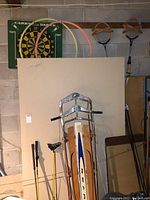 Photo showing Sears metal sled with wood seat, mounted dartboard, badminton rackets, and hula hoops hanging on wall.