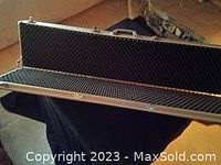 Aluminum rifle case shown open to reveal foam-padded interior, resting on a black cloth.