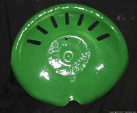 Close-up image of green painted metal tractor seat with ventilation slots and mounting hole.