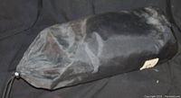 Black cylindrical carrying bag containing the backpacking tent, shown on a dark background.