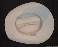 White cowboy hat with a braided decorative band and a small metal charm, showing minimal wear.