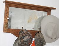 Close-up of wood framed hallway hat rack with etched mirror and four metal hooks holding hats.