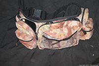 Camouflage accessories belt with several zipped pouches laid on black fabric background.