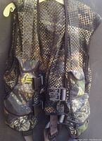 Front view of camouflage hunters safety vest with harness showing mesh fabric, brand logo, and adjustable strap buckles.