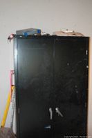 Closed view of tall black metal storage cabinet with locking handles and minor surface scratches.