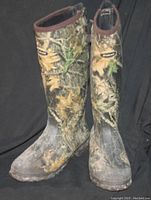 Pair of tall rubber boots with camouflage leaf pattern on black background showing front and side views.
