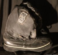 Single side profile of a black SOREL snow boot with a thick sole and roll-up thigh-high gaiter featuring a branded patch on the side
