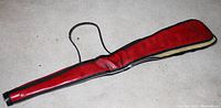 Leather soft shotgun case with red interior lining and carrying strap placed on carpeted floor