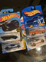 Photo showing four sealed Hot Wheels cars including Batman Batmobile and La Pasta models.