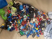 Image showing a large pile of assorted toys and figures on a couch including superheroes, cartoon characters, and other figures.
