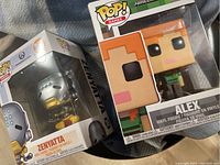 Photo showing two vinyl Pop figures in their original boxes: Zenyatta from Overwatch and Alex from Minecraft.