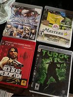 Photo showing four PlayStation 3 games including BlazBlue, Tiger Woods PGA Tour 12, Red Dead Redemption, and Turok with cases in good condition.