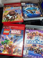 Four PS3 game cases: Little Big Planet, PlayStation All-Stars Battle Royale, LEGO Marvel Super Heroes, and F1 Race Stars