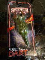 Photo of sealed Stranger Things Squeezable Dart toy in original packaging showing the green creature encased in clear plastic on branded card backing.