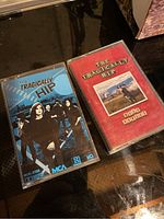 Photo showing two The Tragically Hip cassette tapes, one blue cover with band photo and MCA logo, the other red cover labeled 'Road Apples' with rural landscape image.