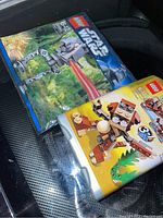 Photo showing two sealed LEGO sets placed on a car seat: one Star Wars AT-ST Walker set and one LEGO Creator set.